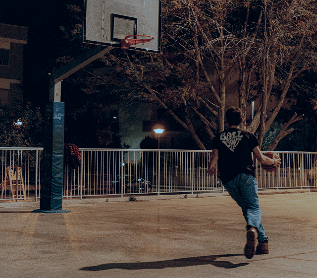 En kille spelar basket på en upplyst basketplan sent på kvällen